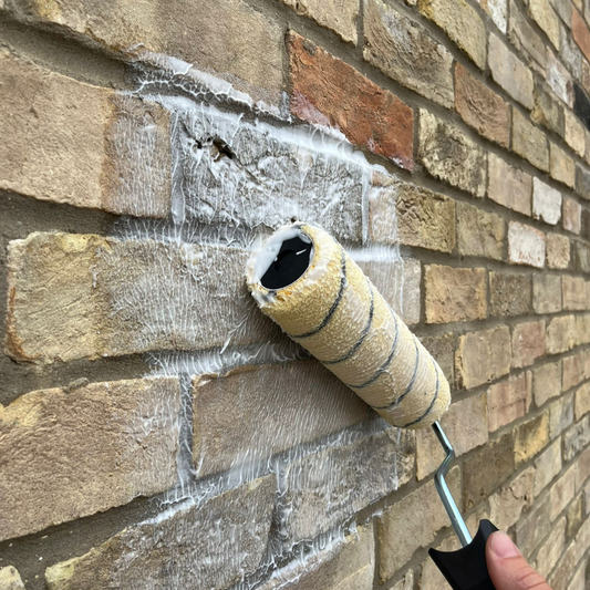 Roller applying brick sealer cream to exterior masonry wall for damp protection.